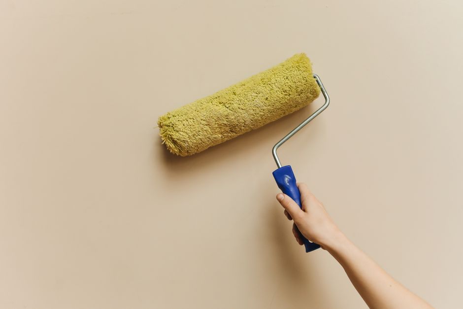 A hand rolling paint onto a beige wall.