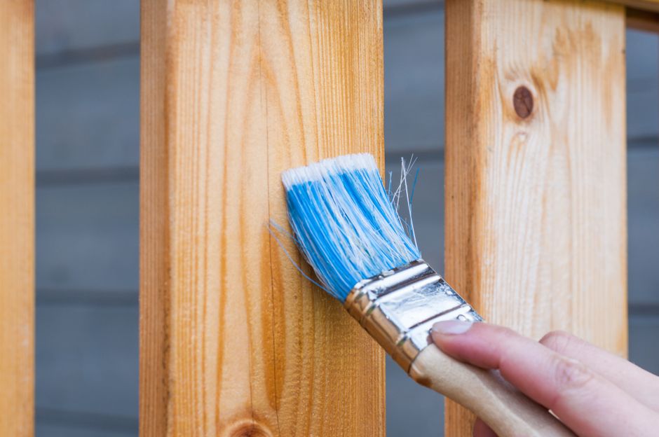 A hand brushing blue paint onto a wooden board outdoors.