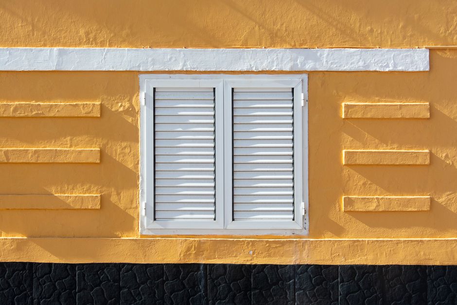 Close-up of a yellow painted wall with white shutters.