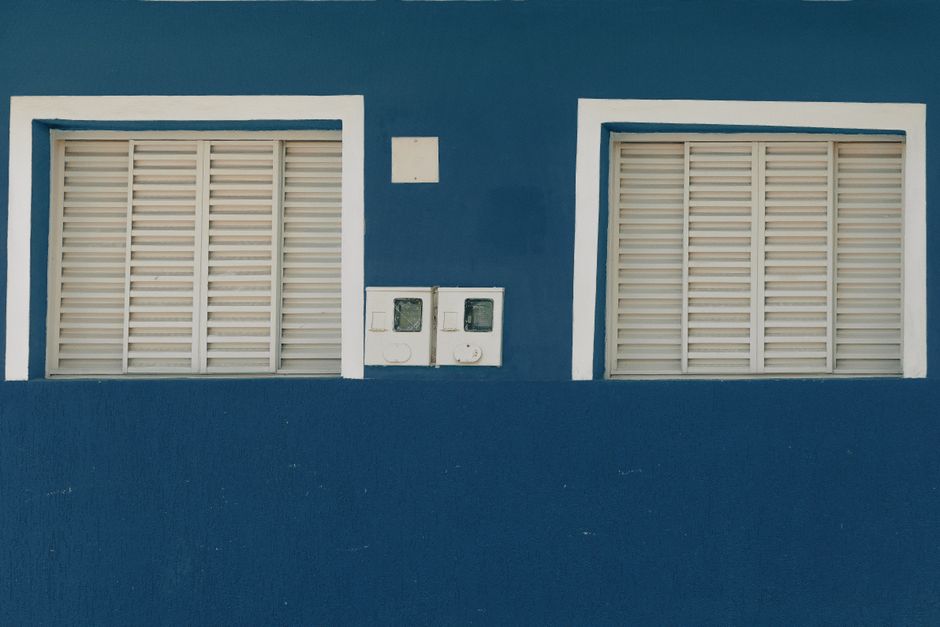 A blue painted wall with two white shuttered windows.