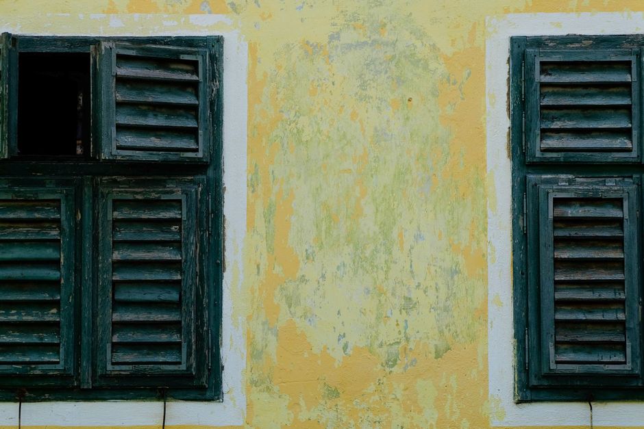 Wooden louvered shutters on a faded yellow wall.